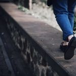 Person walking on a stone ledge outdoors, wearing denim pants and black shoes.