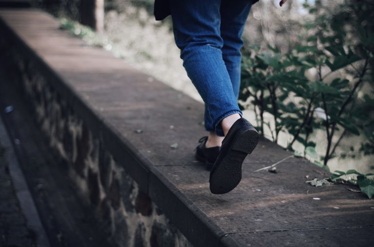 Person walking on a stone ledge outdoors, wearing denim pants and black shoes.